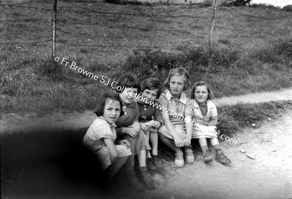 GROUP OF CHILDREN SITTING AT ROADSIDE